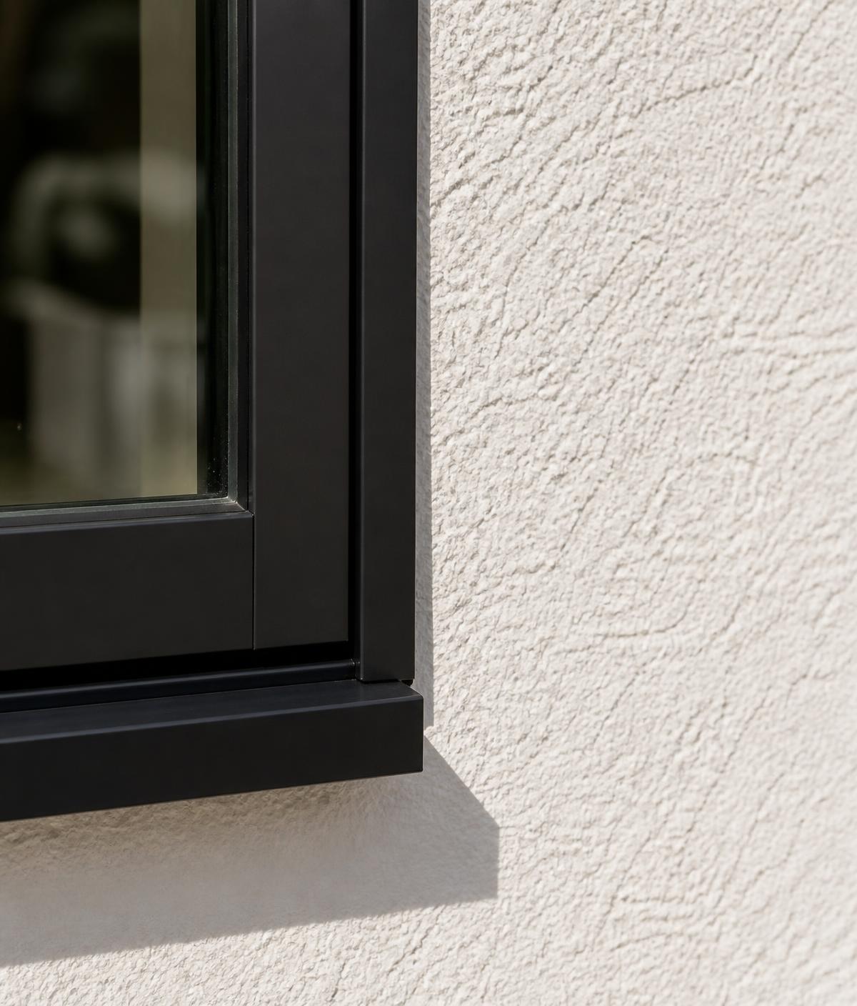 Detail of a black aluminum window frame meeting white stucco